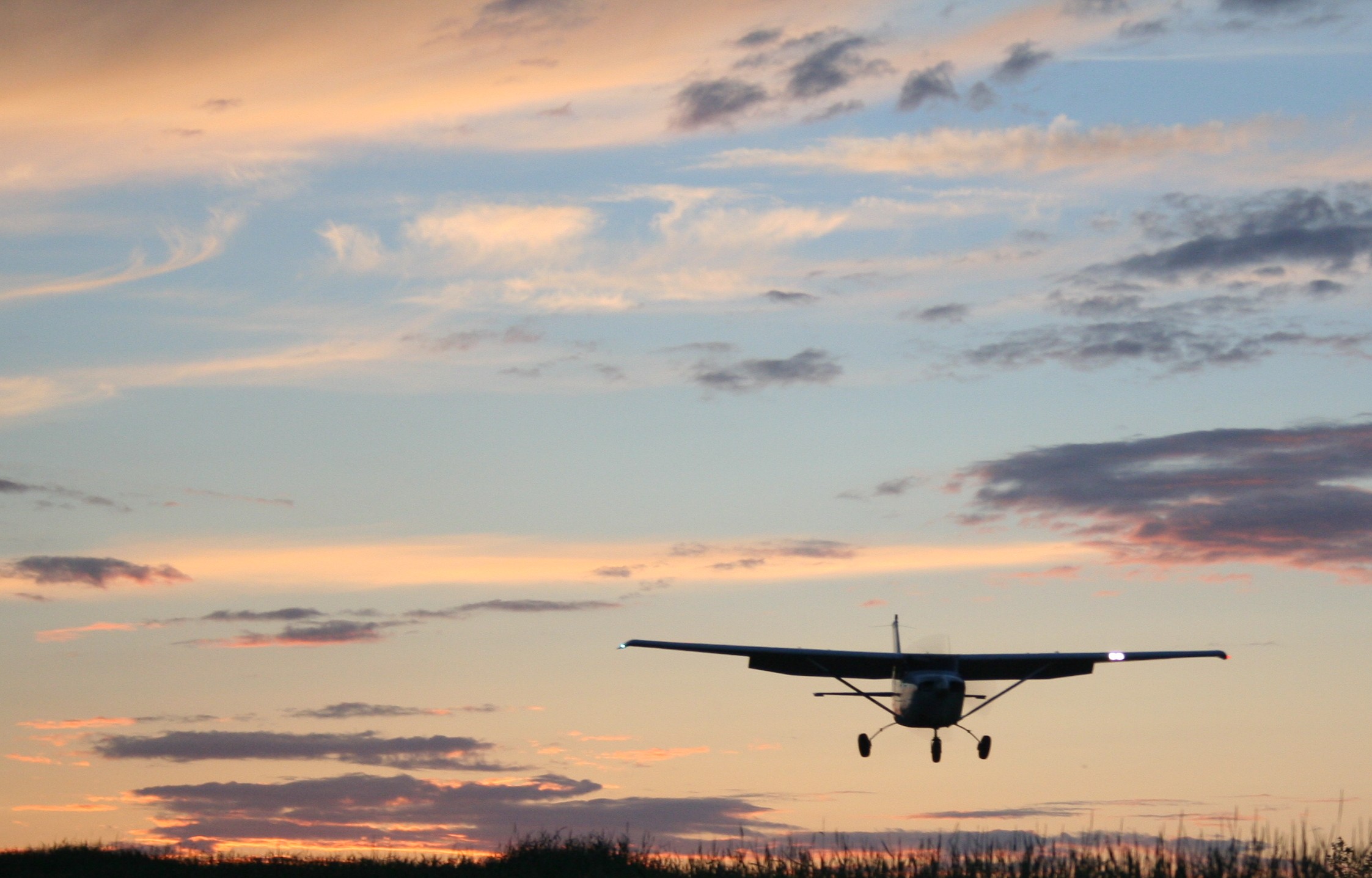 A single engine aircraft flying close to the ground near sunset.