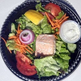 A salmon filet served with fresh local greens and vegetables by The Cod Squad.