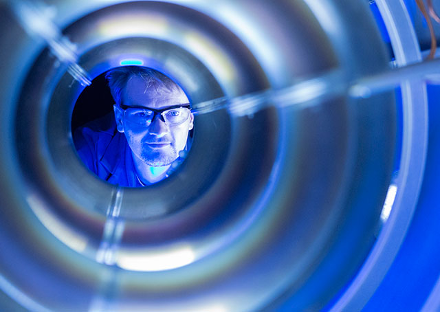 Compact fusion program manager Tom McGuire looks into the T-4 chamber, which is the fourth iteration of the Skunk Works’ compact fusion reactor experiment. The circular magnetic coils shown are critical to containing the hot plasma used to generate the fusion reaction. This experiment will shed light on the feasibility of full size reactors by testing the plasma confinement at lower energies. Eric Schulzinger photo courtesy of Lockheed Martin Corporation.