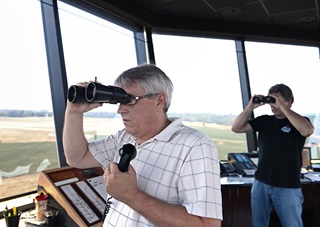 Air traffic controllers Todd Johnson, left, and Steve Till use binoculars to survey the airspace at Frederick Municipal Airport. Photo by David Tulis/AOPA.