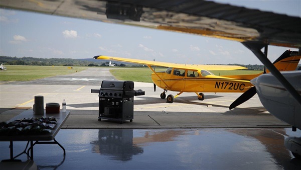 A staged photoshoot at AOPA's NACC with 15-20 "flying club members" interacting in scenarios such as BBQ, flight planning, group watching video, washing airplane, etc.