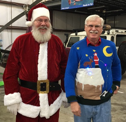 Santa, who flew a red, white, and blue Van's RV-7A, stands with Ed Nabb Jr. in a hangar at Bay Bridge Airport prior to departing for Tangier Island. Nabb, whose father founded the Holly Run, has aggressive taste in Christmas sweaters. Photo courtesy of Joe Kildea.