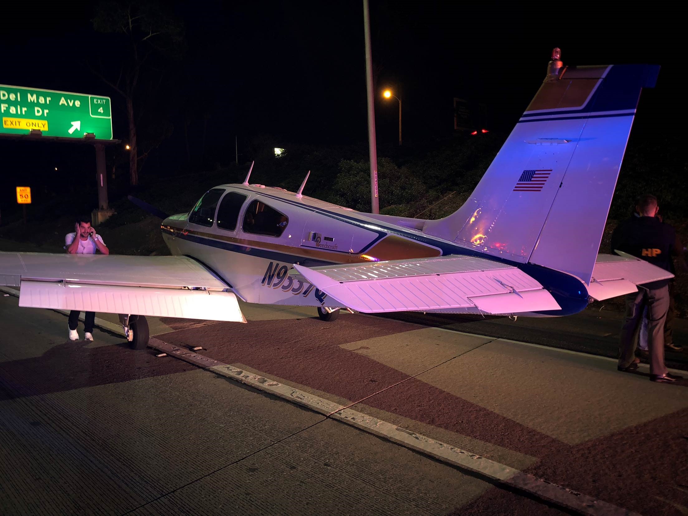 Pilot Izzy Slodowitz talks on a cellphone after surviving a night emergency landing on a Costa Mesa, California, highway in a Beechcraft Bonanza Jan. 28. Photo courtesy of Capt. Chris Coates of Costa Mesa Fire and Rescue.