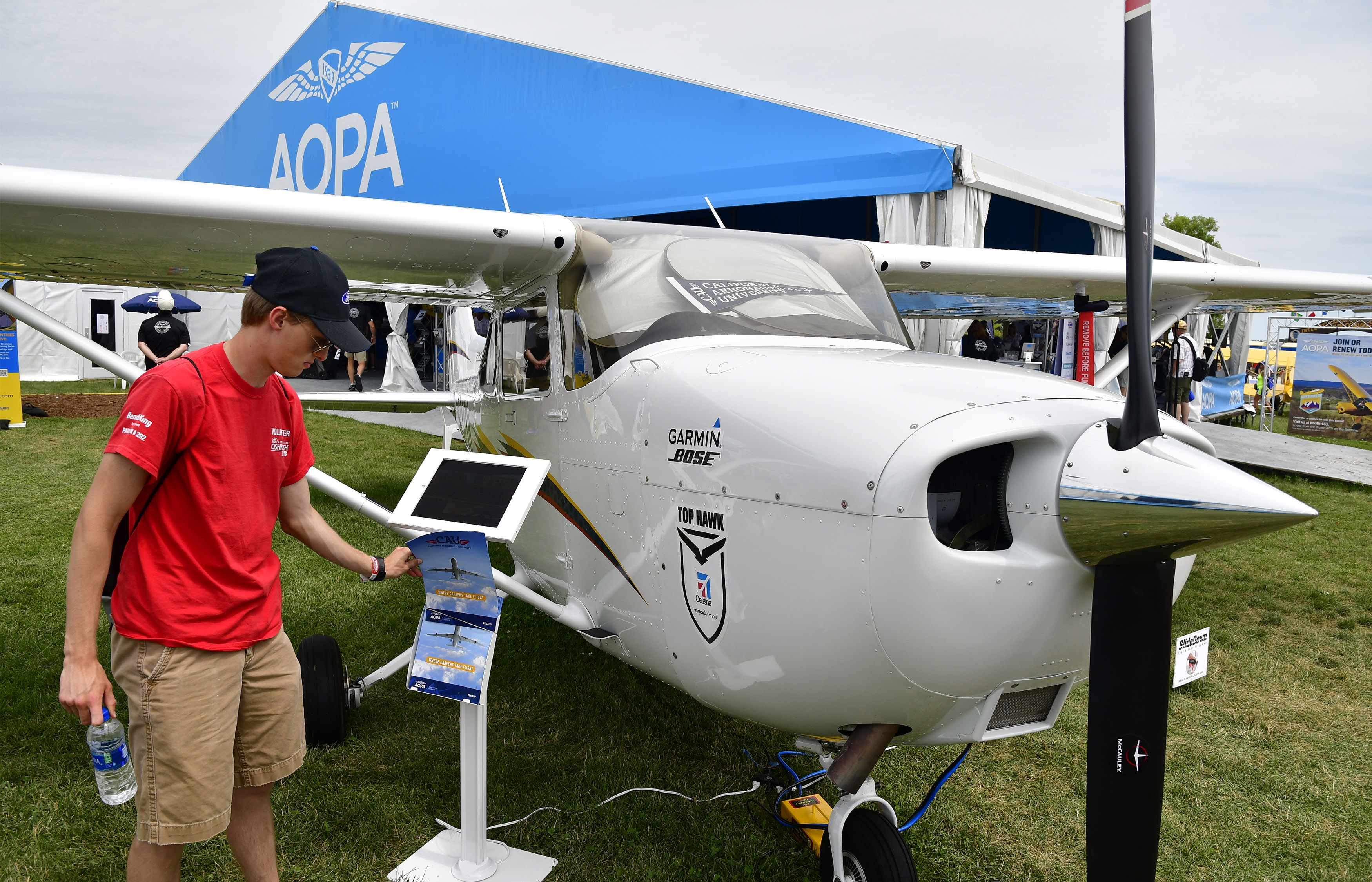 A student checks out a brochure near the California Aeronautical University's Top Hawk Cessna 172 on the AOPA campus during EAA AirVenture in Oshkosh, Wisconsin, July 25, 2018. Photo by David Tulis.