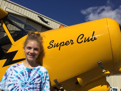 Piper, the daughter of U.S. Marine Corps pilot Benjamin DeBardeleben, poses for a photo next to the AOPA Sweepstakes Super Cub during the AOPA Gulf Shores Fly-In. The youth was named in honor of her grandfather Nelson, who ignited the aviation flame with a Piper Cub flight for her dad. Photo by Alyssa J. Cobb.
