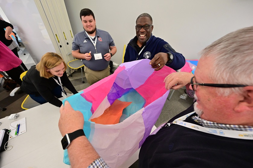 High school educator Eddie Carr of New York smiles as he helps his teammates make a hot air balloon from tissue paper during an AOPA ninth grade curriculum workshop. Photo by David Tulis.