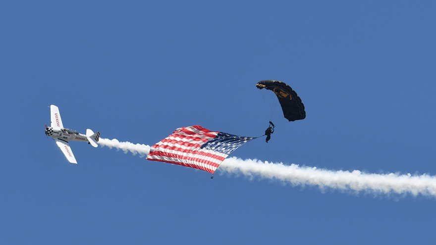 With smoke on, a North American T-6 circles the skydiver landing the American flag to open one of the 2019 Sun 'n Fun International Fly-In and Expo's daily airshows. Photo by Mike Collins.