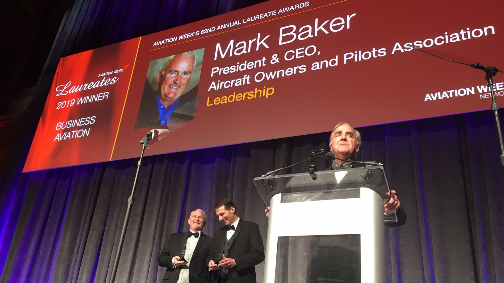 William Garvey, editor in chief of Business and Commercial Aviation magazine (at podium), congratulates AOPA President Mark Baker (left) for winning the Leadership Laureate in the Business Aviation category during the sixty-second annual presentation of the Aviation Week awards. Jim Alpiser, Garmin's director of aviation aftermarket sales (next to Baker), had just been awarded the Laureate for Electronics/Avionics in the same category. Photo by Tom Haines.