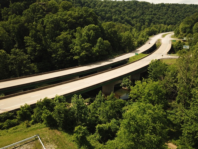 Aerial view over highway winding through green hills.