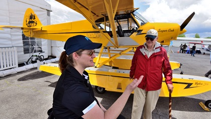 Alyssa Cobb, left, project manager for AOPA's Super Cub Sweepstakes airplane in the background, discusses the airplane with Lowell Powers Jr. of Middletown, Rhode Island. A 50-year AOPA member, he owns a Beech Baron and has flown 200 missions for Angel Flight Northeast. Photo by Mike Collins.