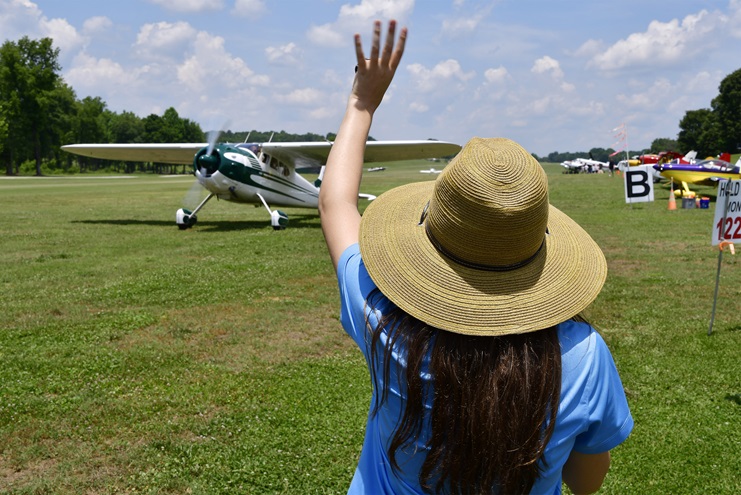 Young Aviators Fly-In co-founder Cayla McLeod waves goodbye to a departing Cessna 195 pilot at Triple Tree Aerodrome in Woodruff, South Carolina. Photo by David Tulis.