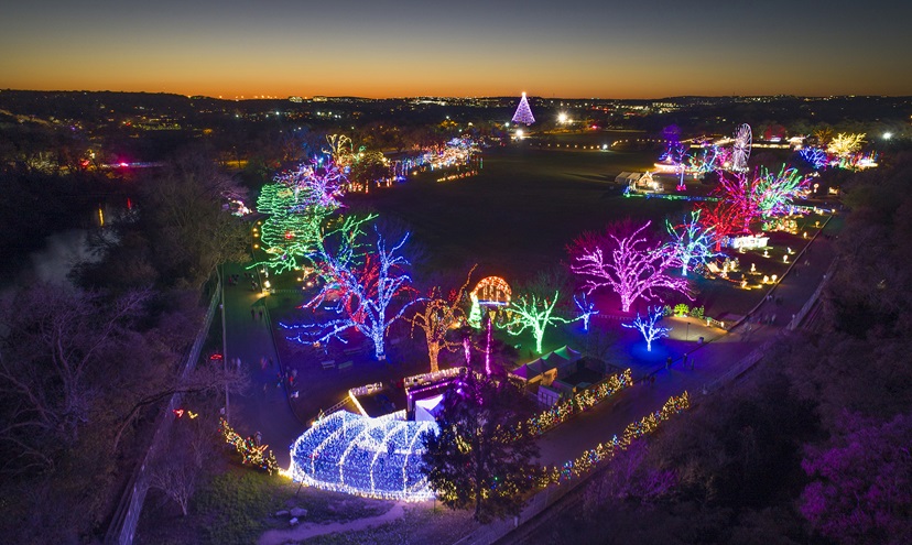 This photo shows the Austin, Texas. Trail of Lights holiday display, with the Zilker Tree in the background, right. The photo was made with the DJI Phantom 4 Pro, about eight minutes past evening civil twilight.  It is a two-second exposure at 100 ISO and f4. Photo looks southwest towards the sunset. Photo by Zach Ryall.