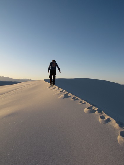 A hiker walks across the top of a dune at White Sands National Park. Photo courtesy of the National Park Service.