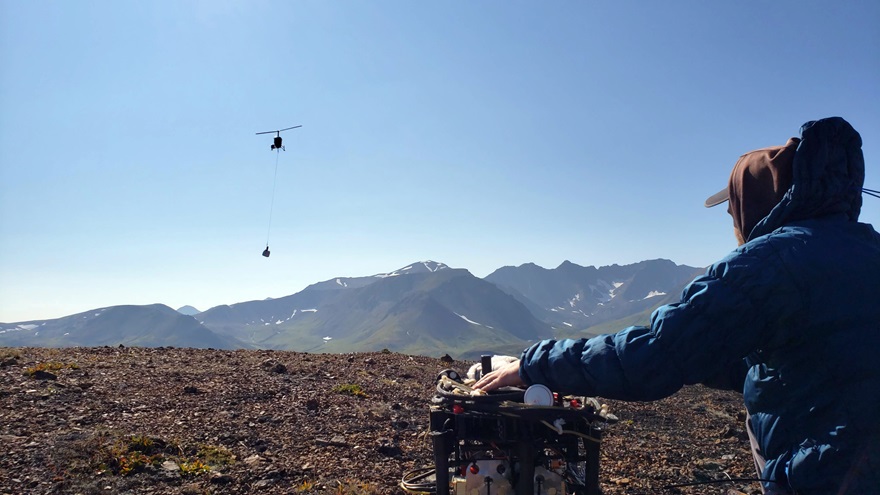 A Robinson R44 helicopter transports survey gear into a remote field location where unmanned aircraft crews  performed magnetometer surveys. Photo courtesy of Pioneer Exploration Consultants.