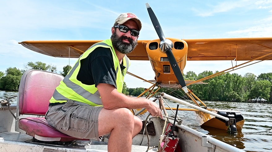 EAA Seaplane Base volunteer Tom Scott pulls a Piper Super Cub on floats to open water. Scott, who is not a pilot, said he loves his job because it is a unique experience in an idyllic setting. Photo by David Tulis.