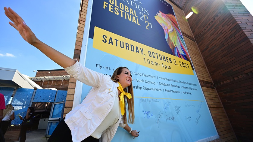 Writer and light sports pilot Jacqueline Ruiz poses near a poster promoting the world's premier Latinas in Aviation festival that featured 15 of Ruiz's 22 pioneer Hispanic women featured in the 2020 book, 