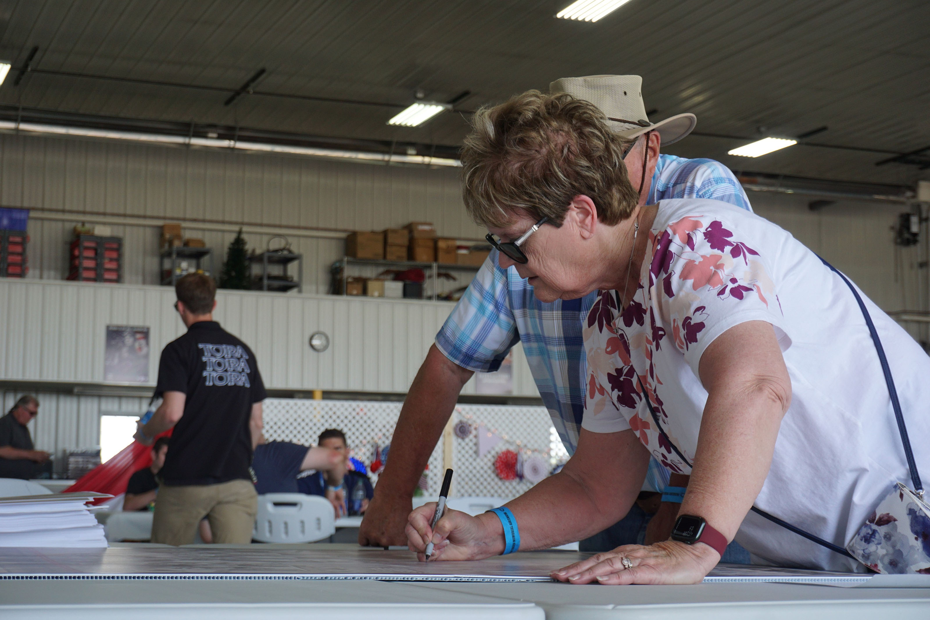 Casey Cain signs her husband’s name, Don Cain, on a poster that veterans were encouraged to sign throughout the event. Photo by Cayla McLeod Hunt.