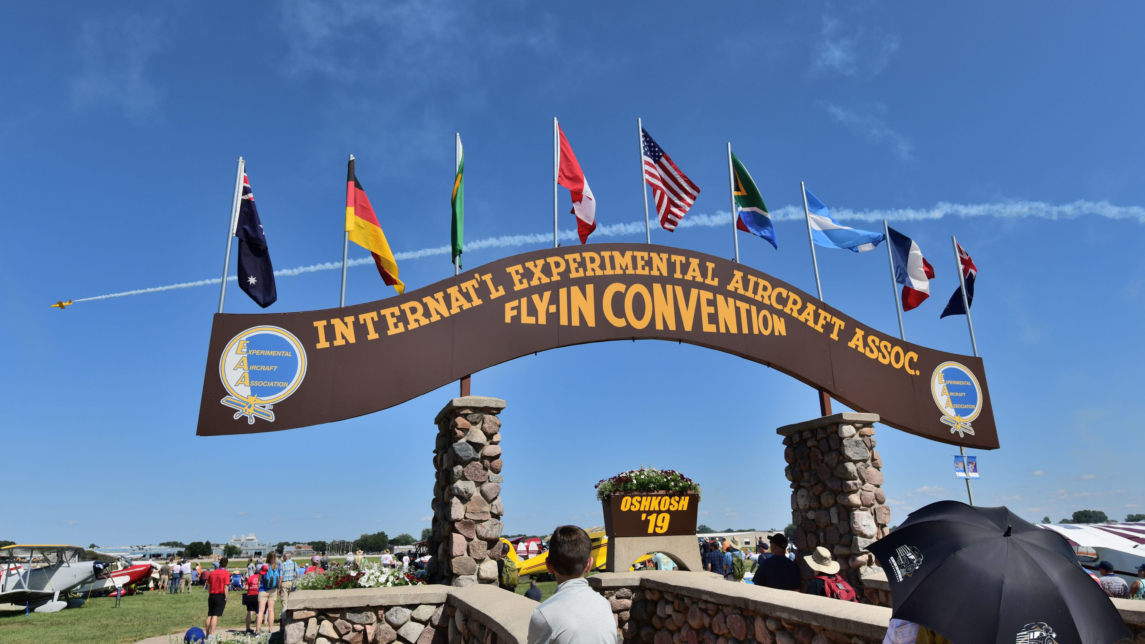 Airshow smoke from a Sonex jet performing in the opening-day EAA AirVenture Oshkosh 2019 airshow creates a background for the legendary brown arch on the fly-in grounds. Photo by Mike Collins.