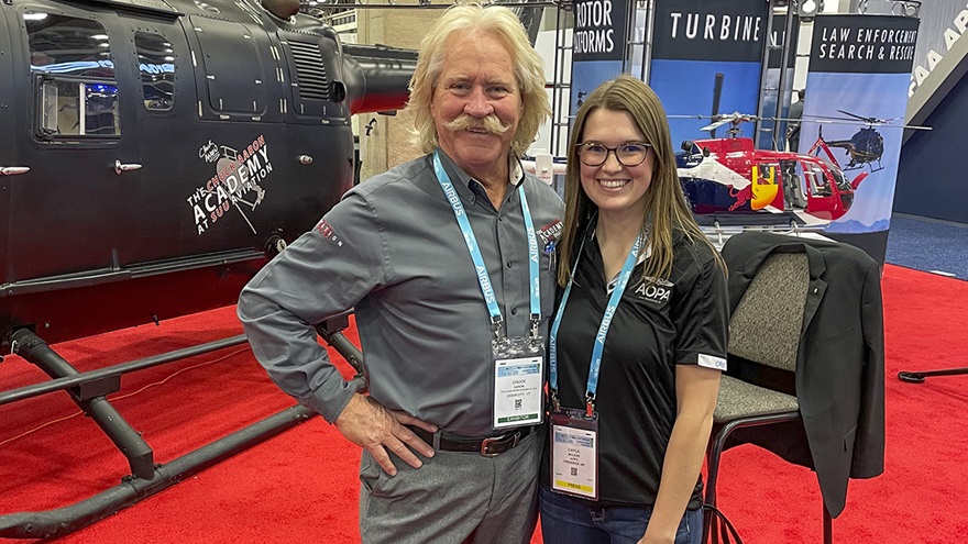 Aerobatic helicopter pilot Chuck Aaron and AOPA Digital Media Assistant Editor Cayla McLeod pose for a photo at the Chuck Aaron Flight Academy at SUU Aviation booth at Helicopter Association International's Heli-Expo in Dallas. Photo by Brian Uretsky.