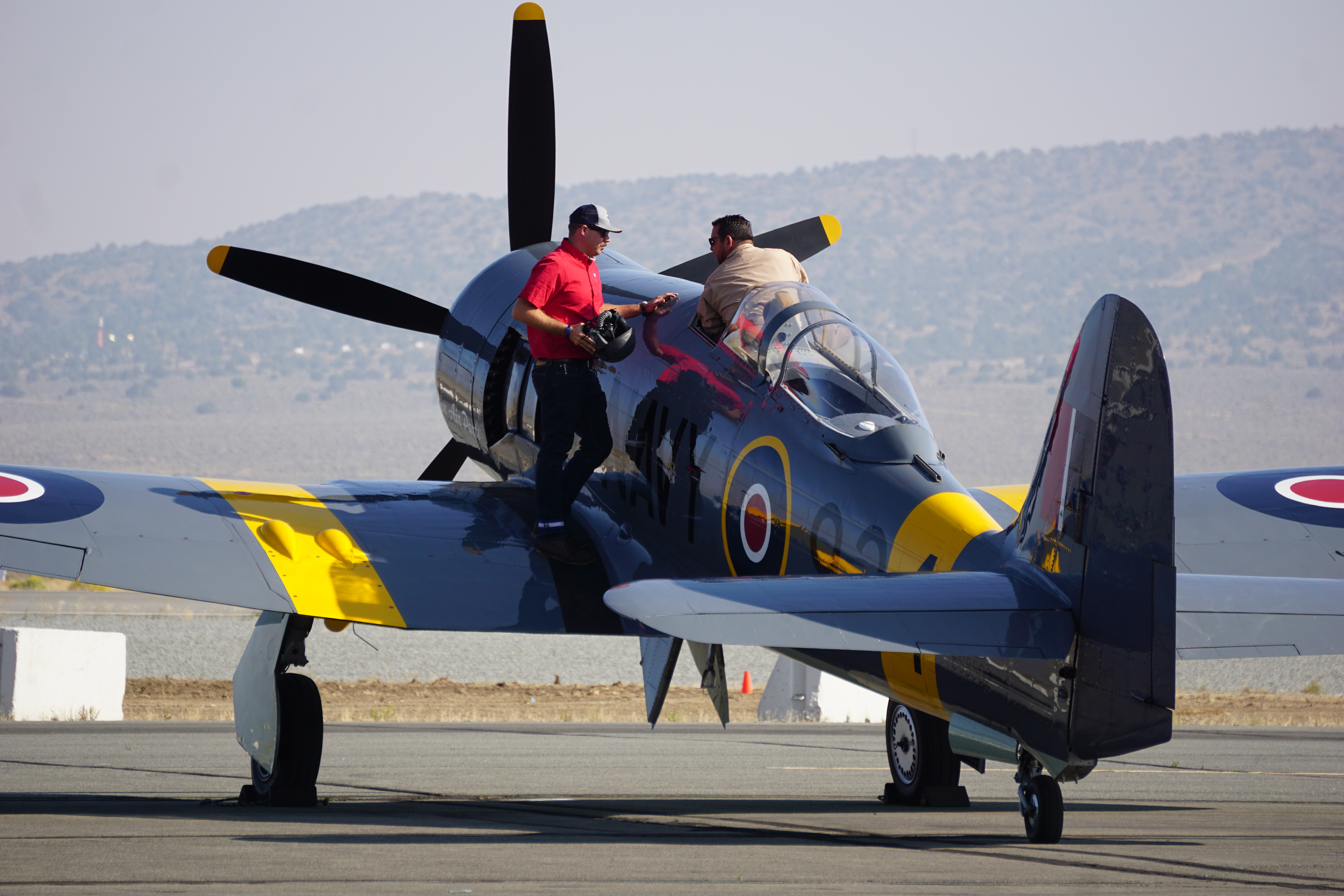 Bernie Vasquez gets situated in the cockpit of a Hawker Sea Fury as teammate Steven Koewler stands by just prior to Saturday’s Unlimited Gold Race. Photo by Cayla McLeod Hunt.