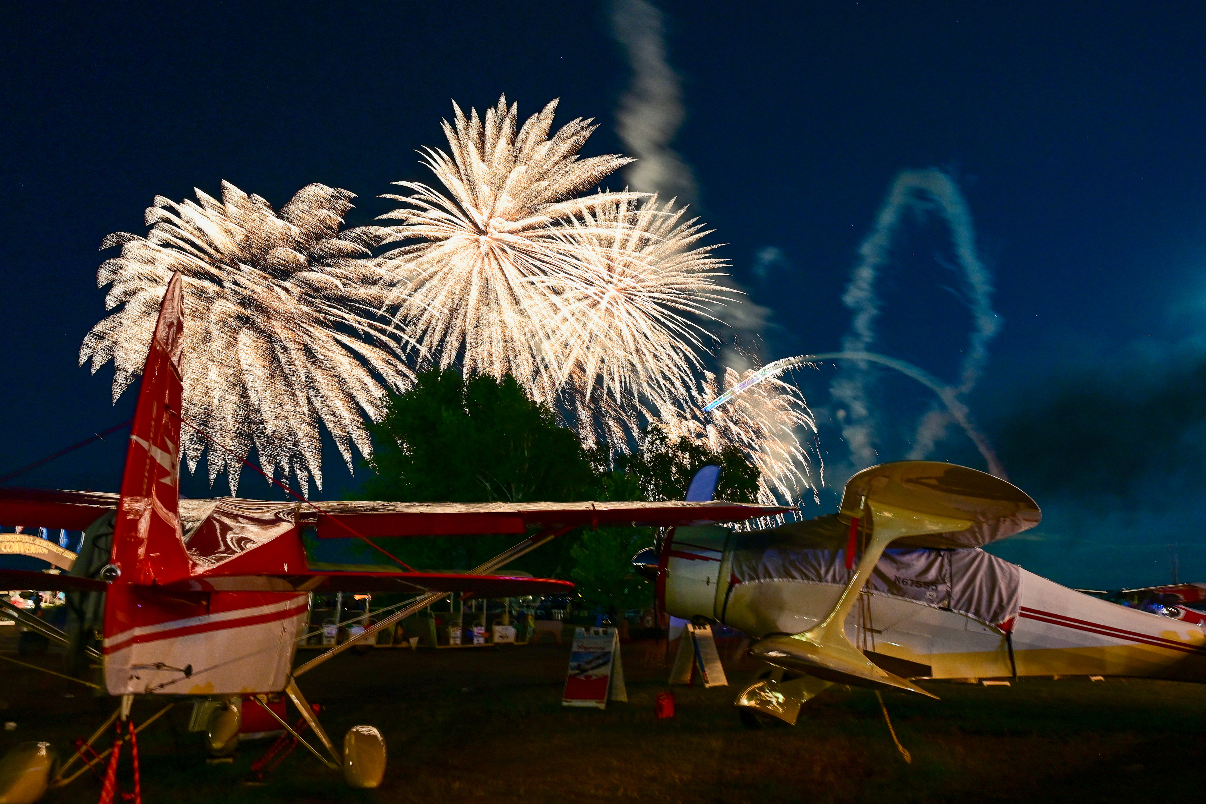 Fireworks explode over a Beech Staggerwing and a Piper Tri-Pacer during the evening airshow. Photo by David Tulis.