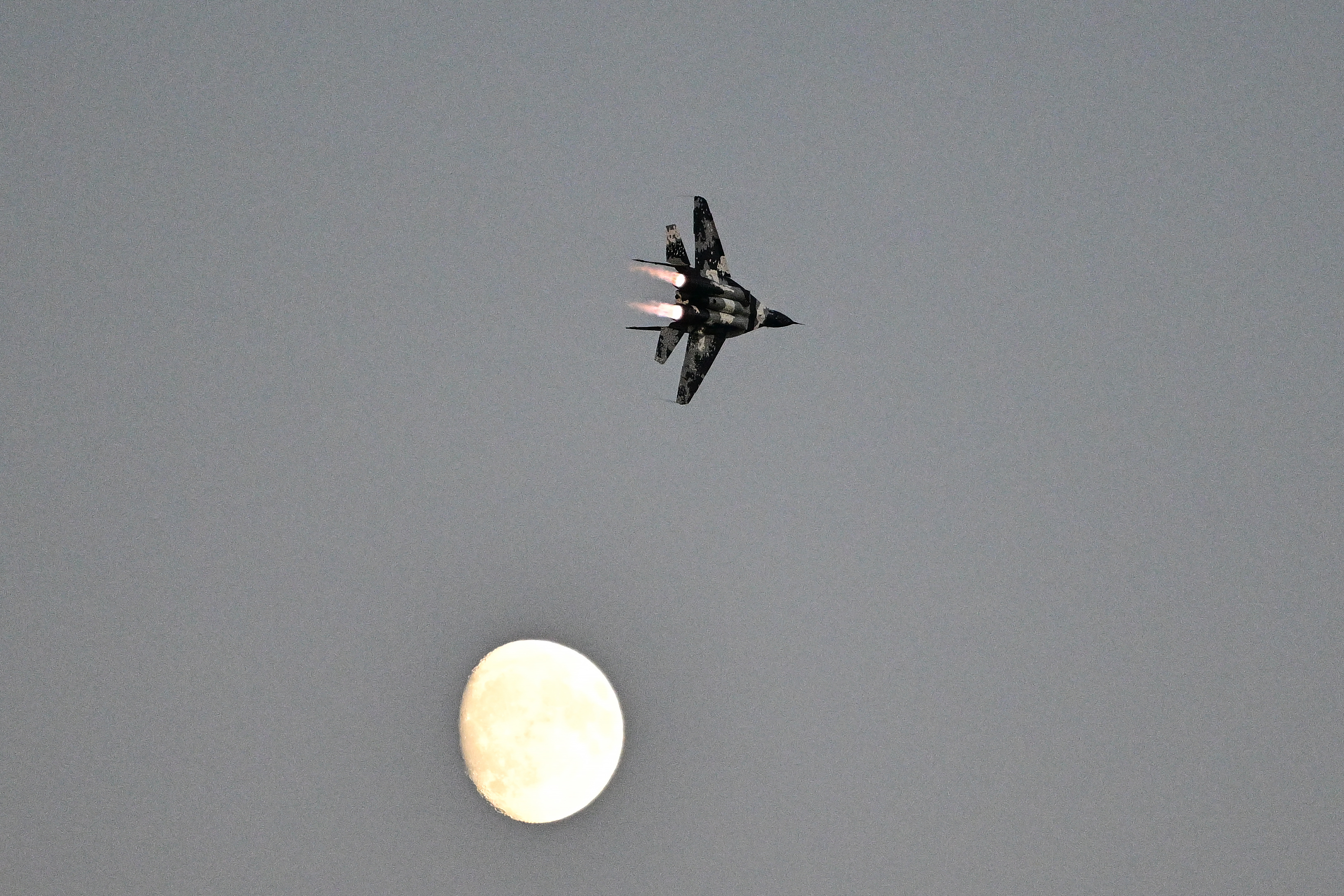 A MiG-29 is framed by a rising moon during the Saturday night airshow. Photo by David Tulis.