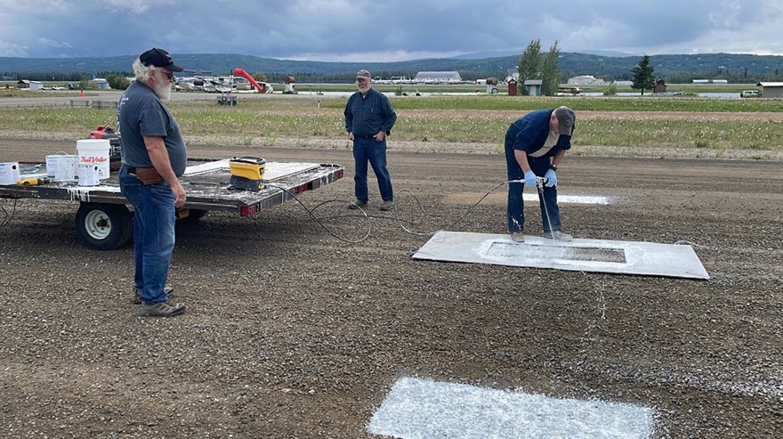 A crew from the Fairbanks General Aviation Association paints the threshold marker denoting the start of a 800 by 25-foot Super Cub strip on the gravel runway at Fairbanks International Airport. Photo by Tom George.