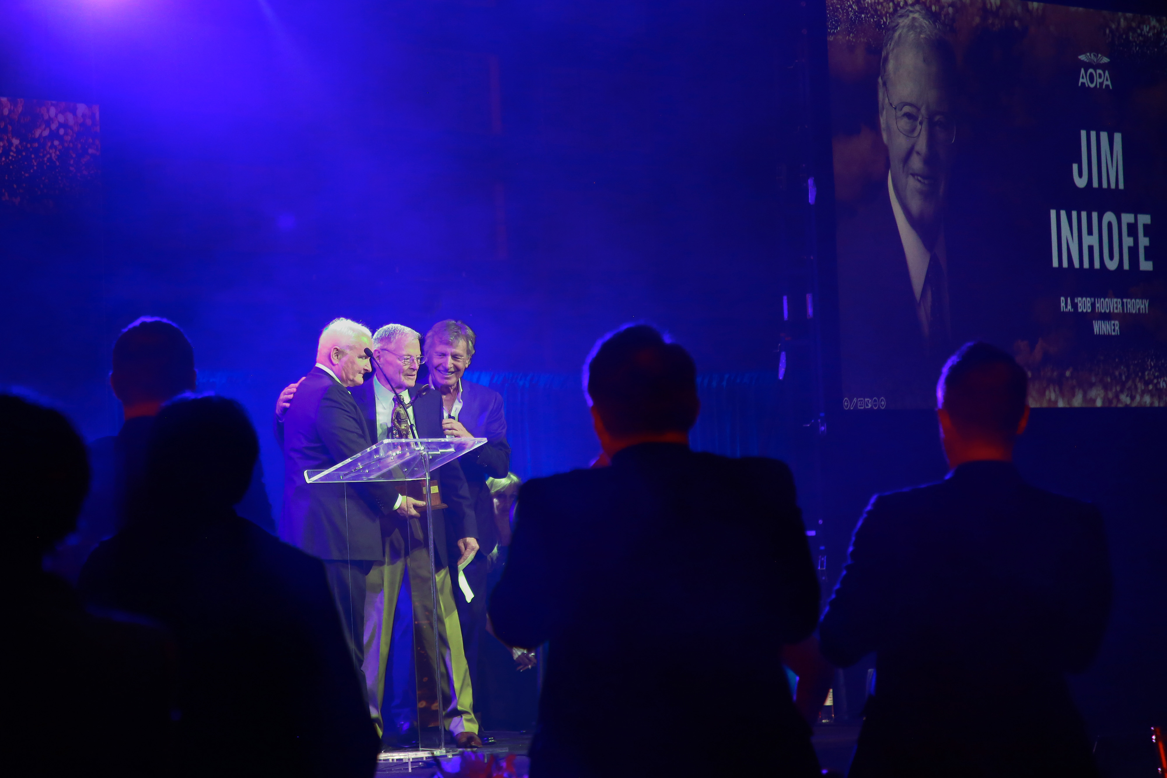 AOPA President Mark Baker and master of ceremonies Sean D. Tucker present retired Sen. James Inhofe with the R.A. 'Bob' Hoover Trophy during the seventh annual reception at Ronald Reagan Washington National Airport in Washington, D.C., March 22.  Photo by Rebecca Boone.