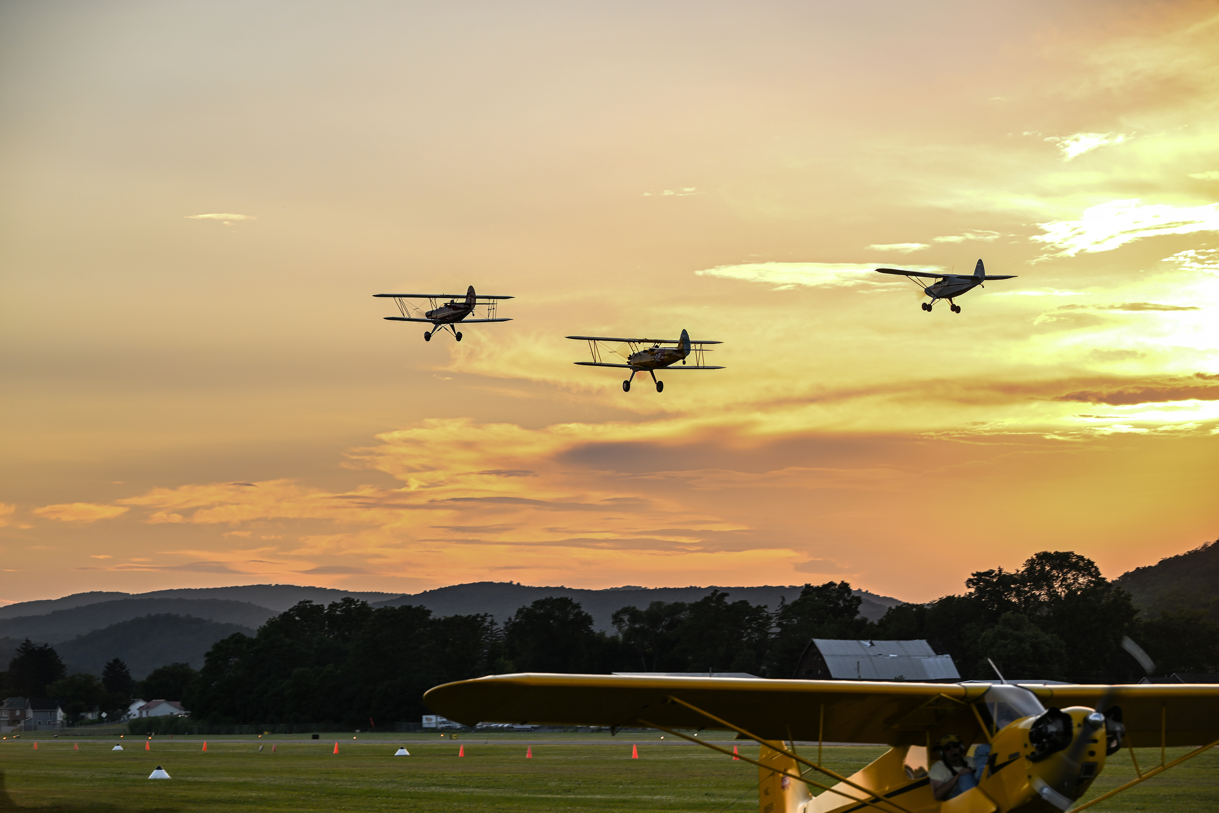 The setting sun provides a backdrop for a pair of biplanes and a Piper PA-16 Clipper on Whittaker landing gear. Photo by David Tulis.