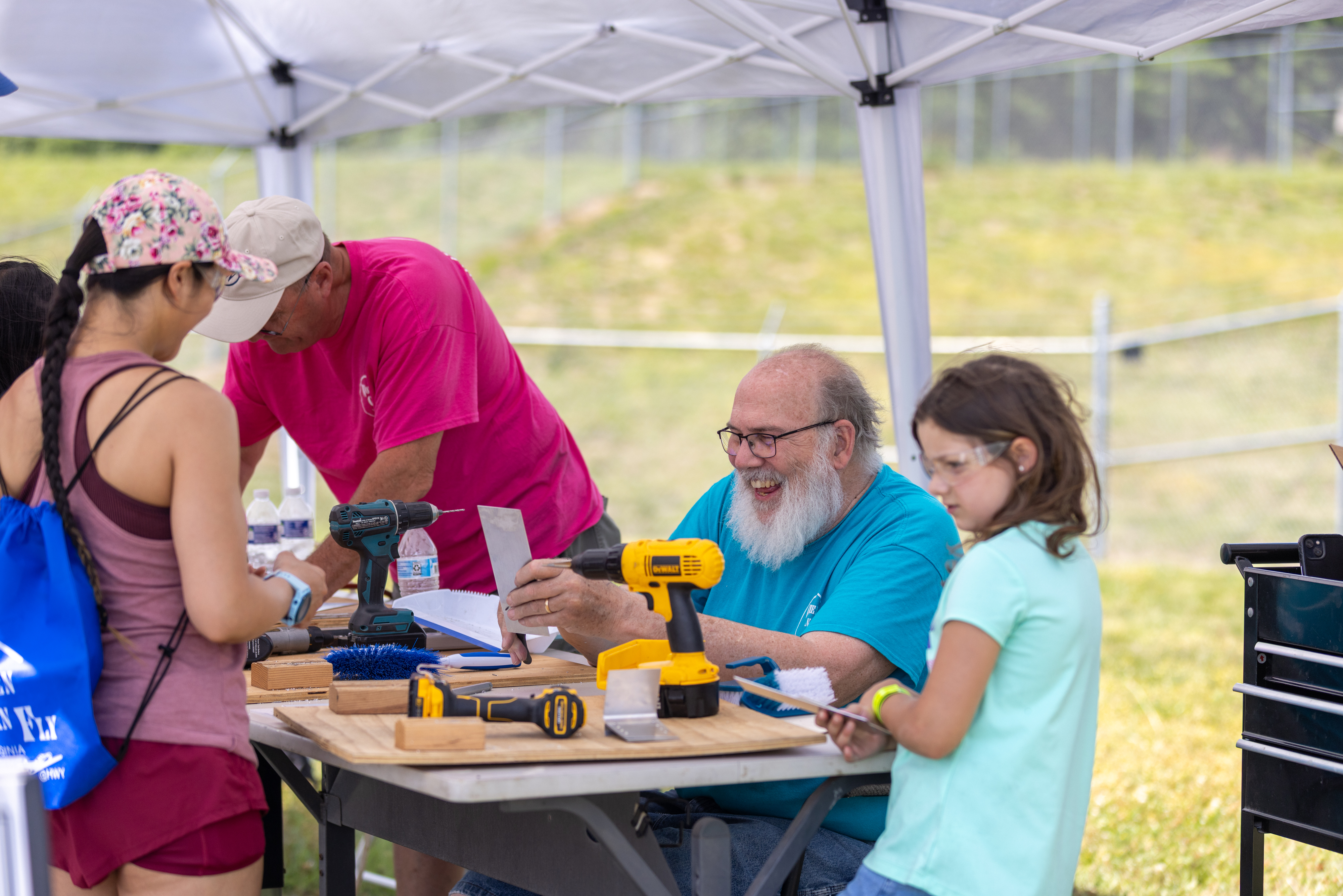 A volunteer at the “Women Can Build” tent teaches attendees how to make a phone stand out of sheet metal. Photo by Rebecca Boone.