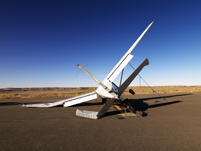 A small, crashed aircraft in a desert landscape. It is on its side with a broken wing and tail. Horizontal shot.