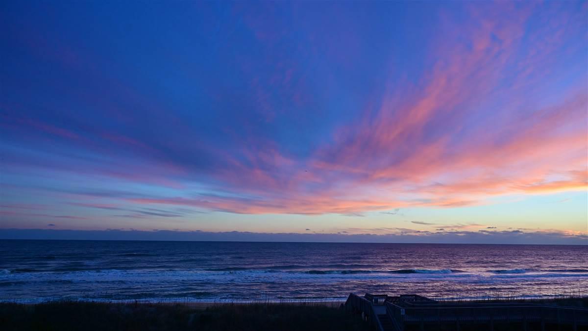 A blue sky ablaze with the beginnings of a pink sunrise frame the beach at Nags Head, North Carolina, near the Wright Brothers National Memorial. Photo by David Tulis