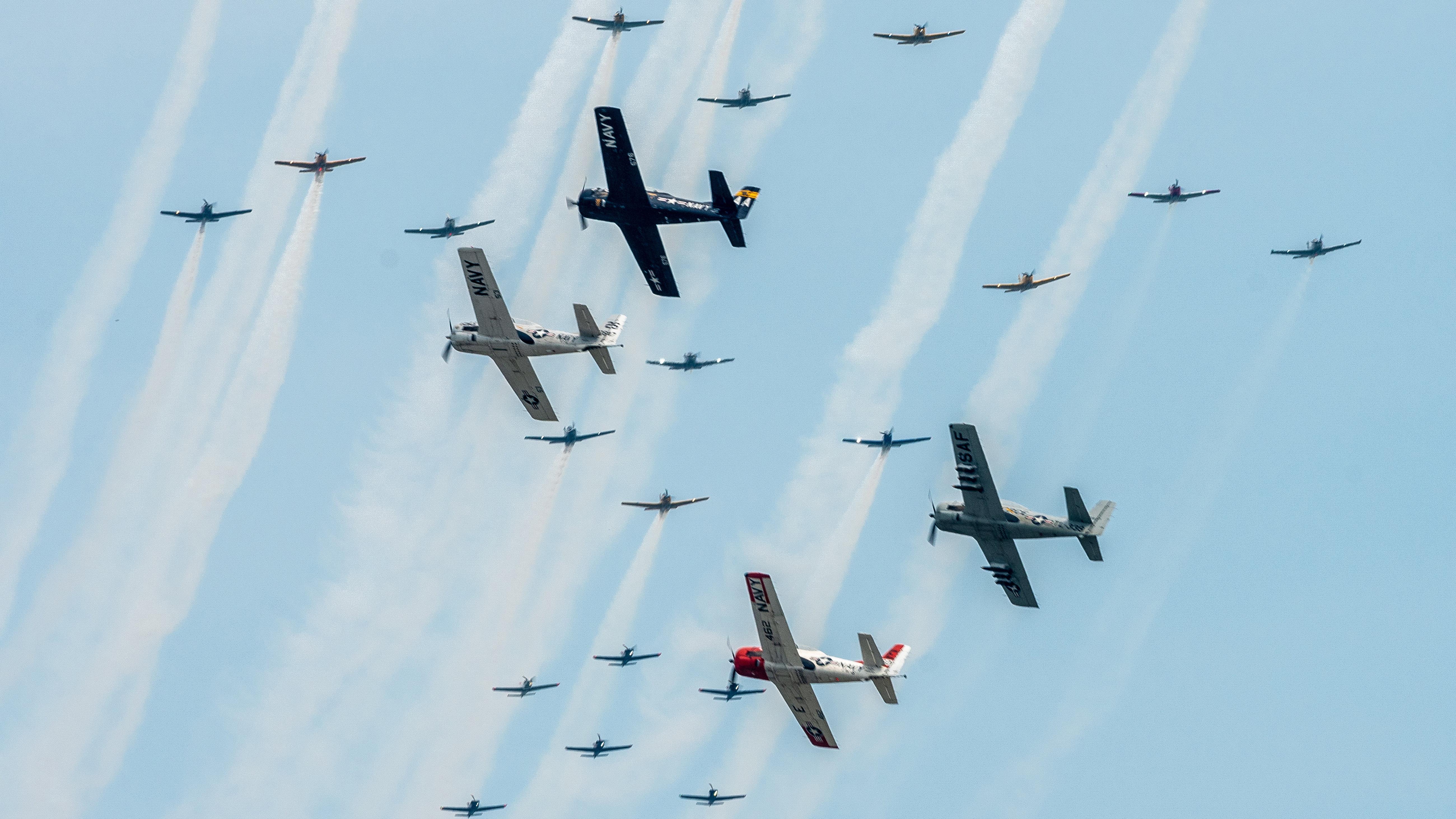 EAA AirVenture Oshkosh 2021. "A photograph may seem like a two-dimensional thing, but there are layers within it. I use telephoto lenses more as a way to compress space between objects than I do to just bring objects closer. I want to create visual relationships between things. The relationships are just as important as the objects. Honestly, a big formation of aircraft is kind of boring in a still photo unless you can find some way to make the image dynamic. In this case, your eye is going to follow the lines of crossing aircraft and be directed around the photo in a circular fashion that creates a dynamic visual flow within a frozen moment in time.”