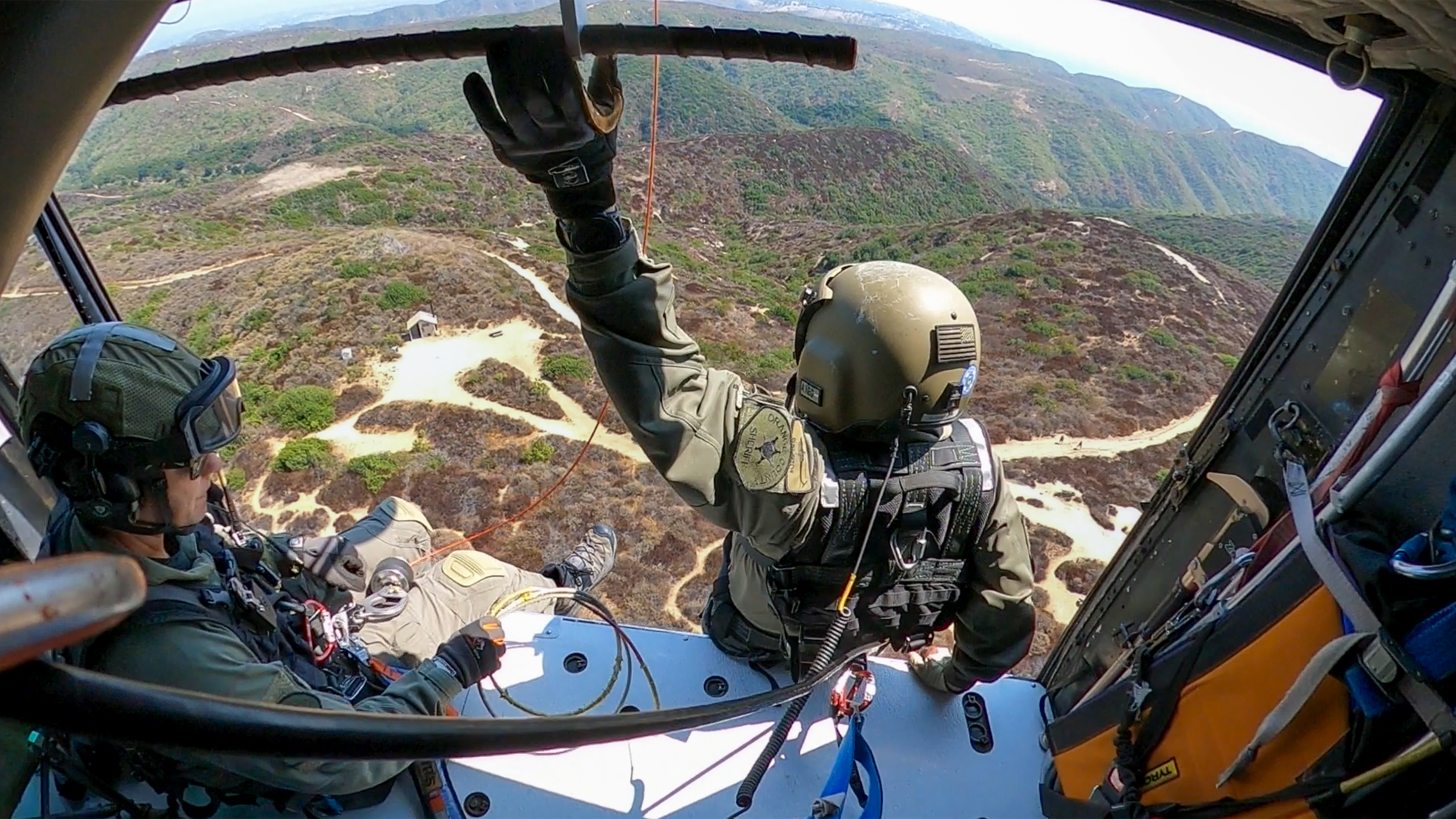 During a training mission, the pilot of Duke 6 hovers the Huey, while unit members stage a rescue operation, hoisting their teammates to and from the ground in the mountains to the south of John Wayne Airport (SNA).