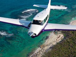 Cherokee airplane flying over blue waters of the Bahamas