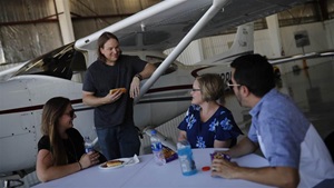 A staged photoshoot at AOPA's NACC with 15-20 "flying club members" interacting in scenarios such as BBQ, flight planning, group watching video, washing airplane, etc.