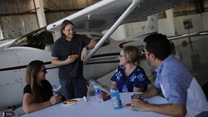 A staged photoshoot at AOPA's NACC with 15-20 "flying club members" interacting in scenarios such as BBQ, flight planning, group watching video, washing airplane, etc.