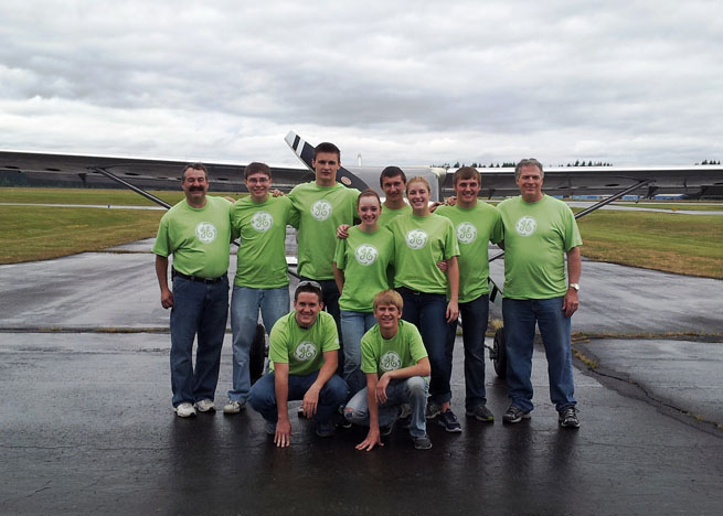 High school students (flanked by Jeppesen President Mark Van Tine on left and GAMA President and CEO Pete Bunce on right) stand in front of the Glasair they helped to build. The airplane taxied on June 27.