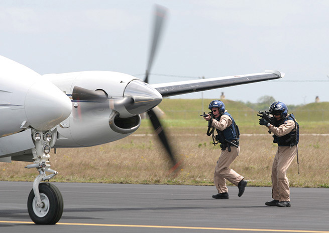 Two CBP Air Interdiction officers stop a suspicious small twin-engine airplane on a runway. Undated photo by James Tourtellotte via Customs and Border Patrol.