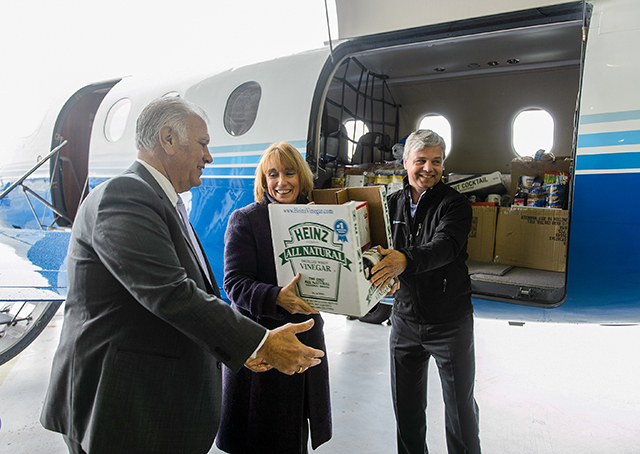 Manchester, New Hampshire, Mayor Ted Gatsas, Gov. Maggie Hassan, and PlaneSense, Inc. President and CEO George Antoniadis unload a Pilatus PC-12 turboprop aircraft with food items donated to the New Hampshire Food Bank during the fractional aircraft company's 2014 food drive. Photo courtesy of PlaneSense Inc. 